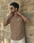 Man wearing a brown shirt and sunglasses against a stone wall
