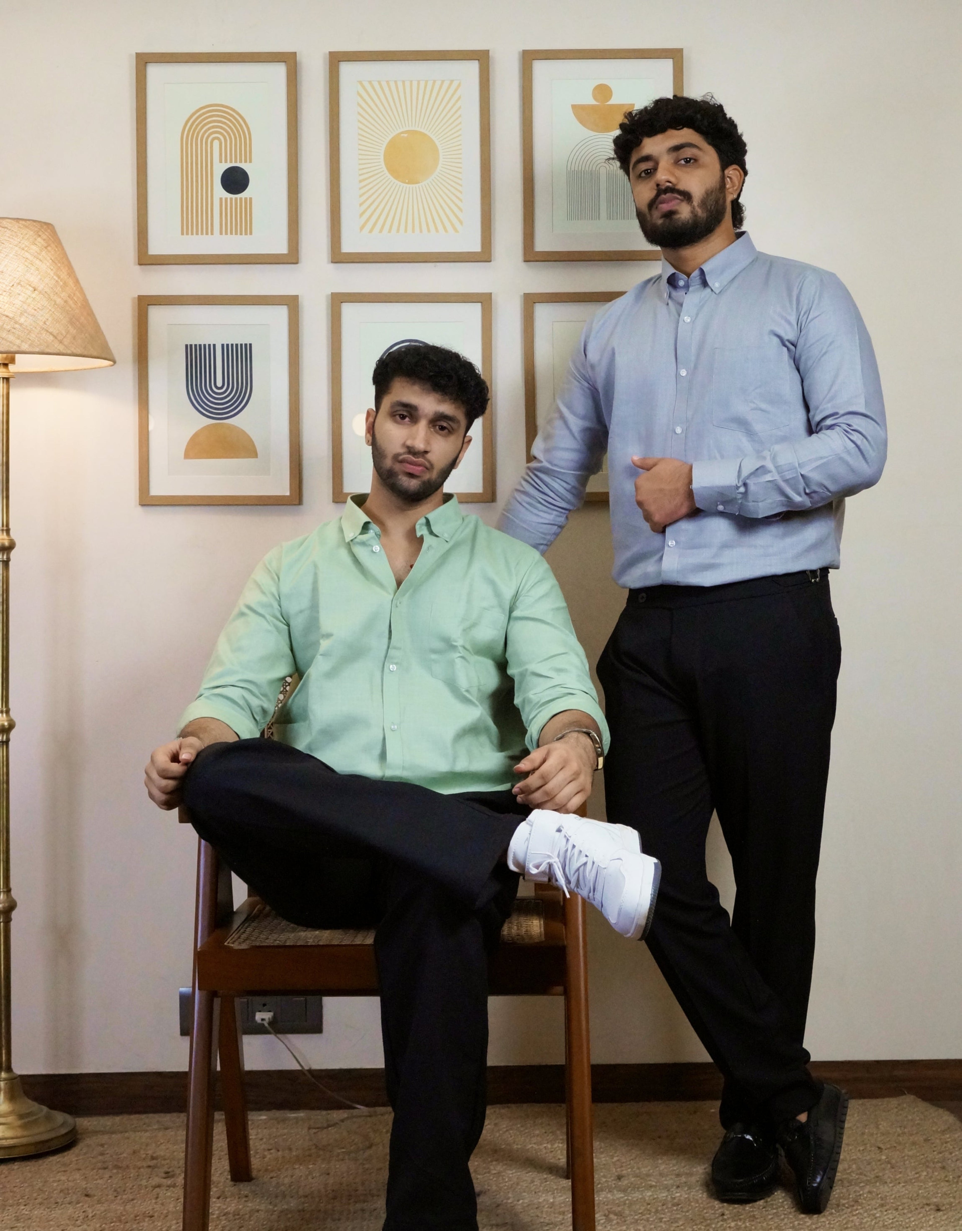 Two men posing indoors with framed artwork on the wall.