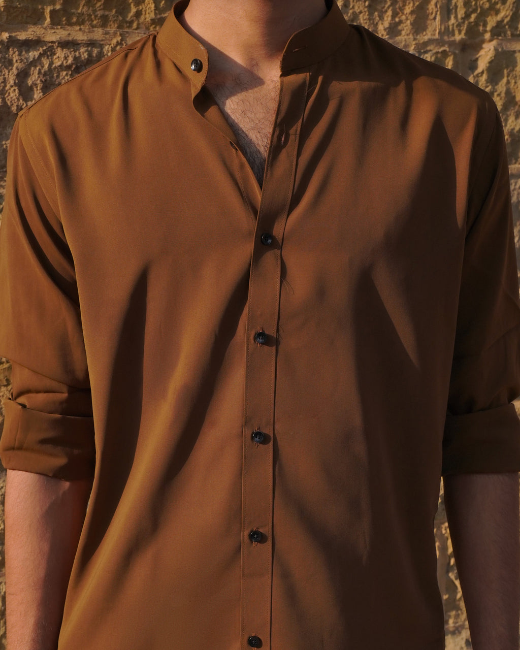 Brown button-up shirt worn by a person against a textured wall.