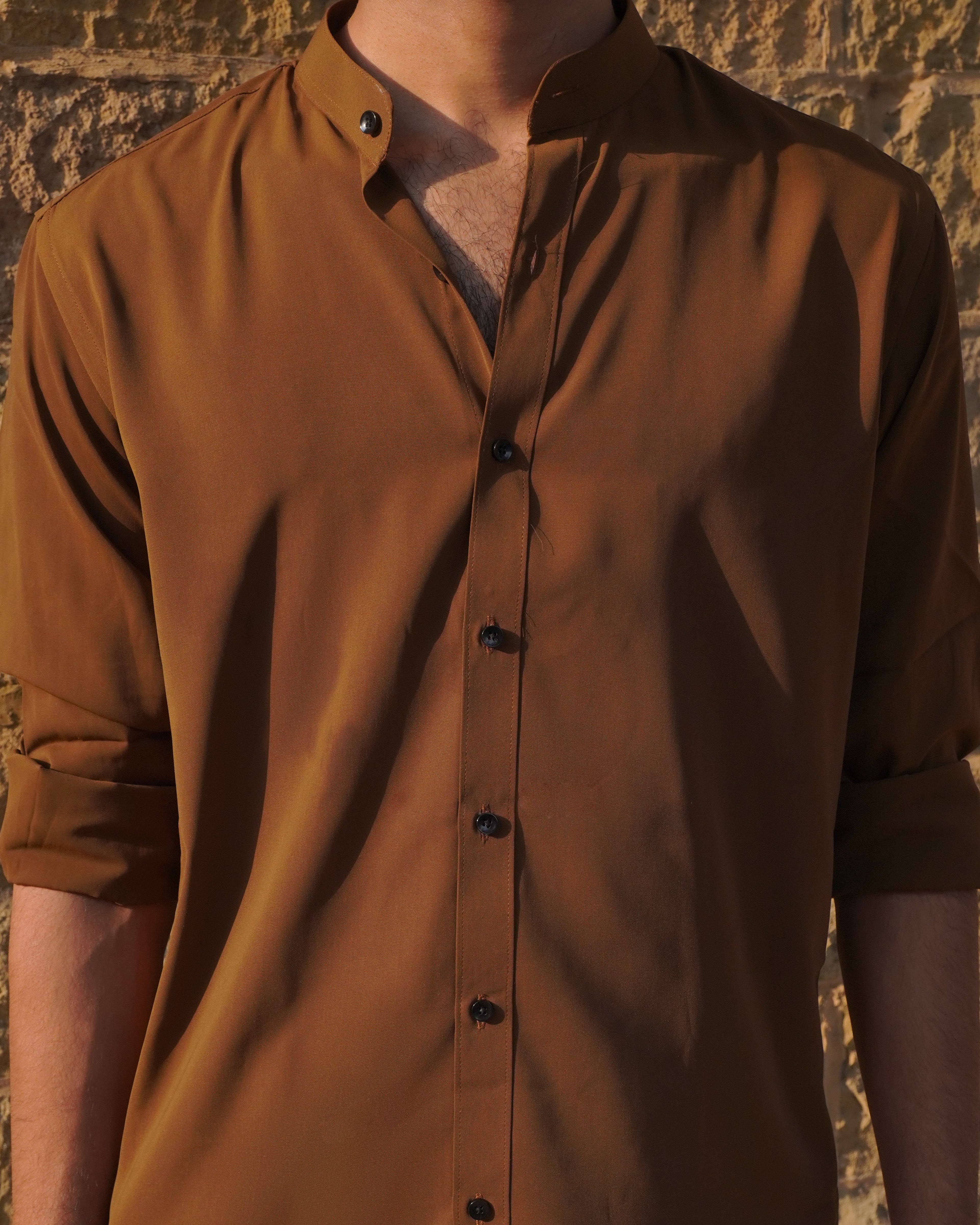 Brown button-up shirt worn by a person against a textured wall.