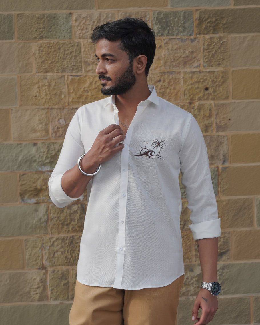 Man wearing a white shirt with a logo against a stone wall.