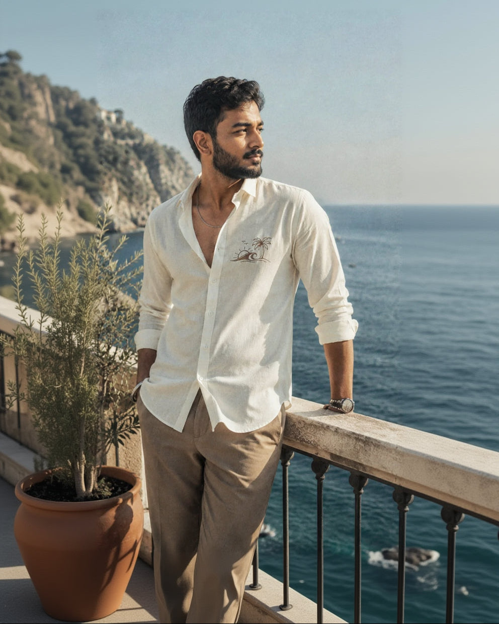 Man standing on a balcony overlooking the ocean with mountains in the background