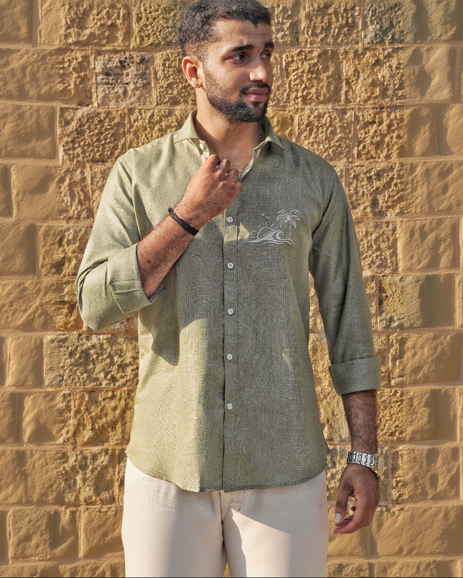 Man wearing a green shirt with a subtle design against a stone wall.
