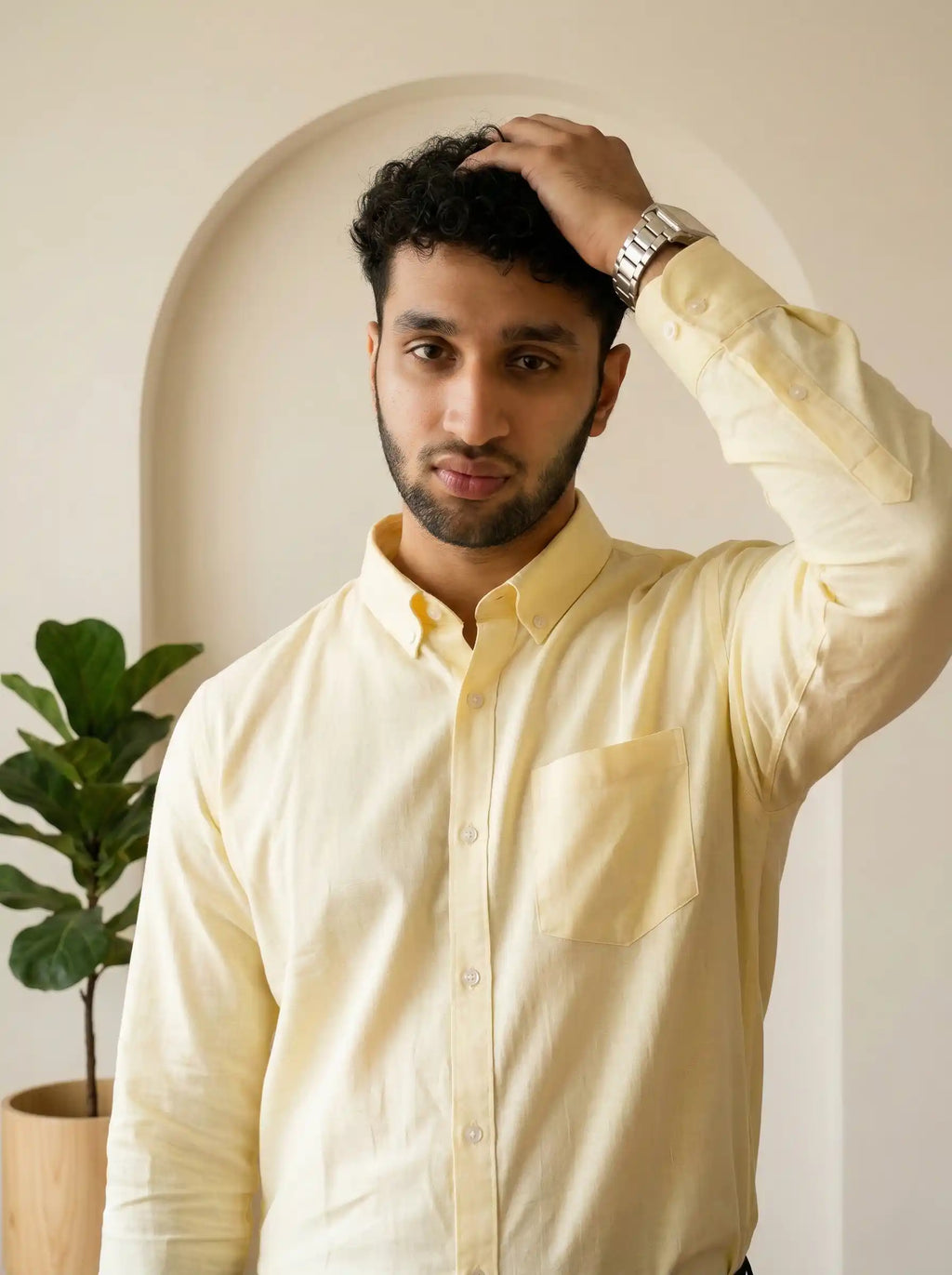 Man wearing a light yellow shirt with a plant in the background