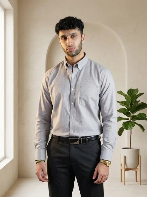 Man wearing a light gray dress shirt and black pants standing in a room with a plant and arched doorway.